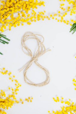 8 Mart bir bahar tatilidir. İpten yapılmış 8 numara beyaz arka planda yatıyor. Yakınlarda sarı bir mimoz dalı uzanıyor.