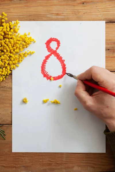 右手用一支古色古香的钢笔在白纸上画一个大大的红色数字8 这张纸放在木板上 左边是一根黄色的模子 — 图库照片