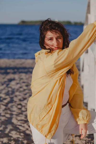 穿着黄色夹克的好女孩躺在沙滩上的白色木制结构上 — 图库照片