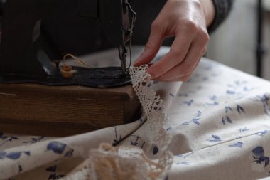 El yapımı terzi. İnce parmaklı kadın örgüyü yakın plan dikiş makinesinde tutuyor. Yakınlarda mavi bir kumaş var.