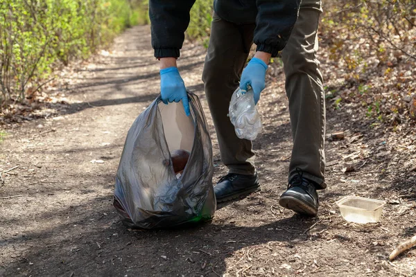 我们把大自然从垃圾中拯救出来 身穿蓝色橡胶手套的生态学家在泡沫中的黑色塑料袋中收集垃圾 — 图库照片