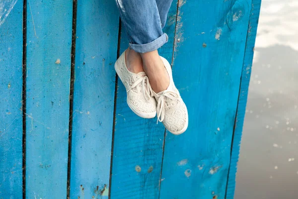 一个女人细长的腿挂在用蓝色木板做的木制防波堤上 他的脚上穿着柔软的白色鞋子 Close — 图库照片