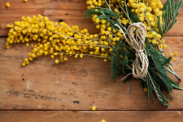 Bahar etüdü. Sarı mimozanın bir dalı tahta tahtalarda yatar. Üstte numara şeklinde bir ip var. 
