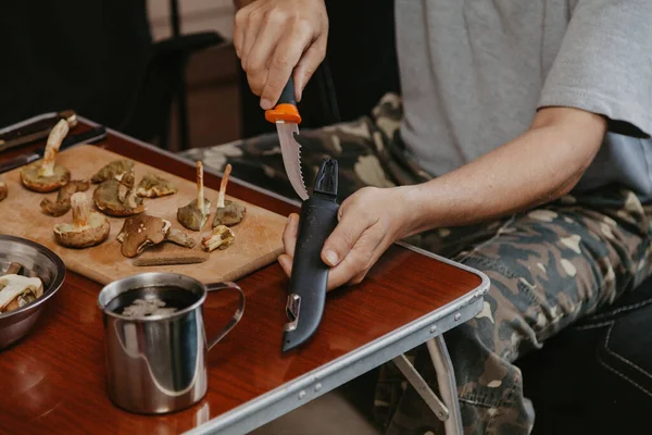 Toplanan mantarların incelenmesi. Tahta bir yaban domuzunun üstünde yenebilir mantar kesen bir adamın elleri.