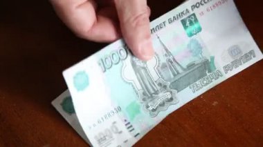 Adam, kahverengi bir masanın üzerinde para sayıyor. Bin Rus rublesi değerinde dokuz banknot.