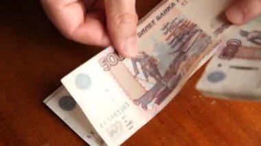 Erkekler kahverengi bir masanın üzerinde para sayıyor. Beş yüz Rus rublesi değerinde on beş banknot.