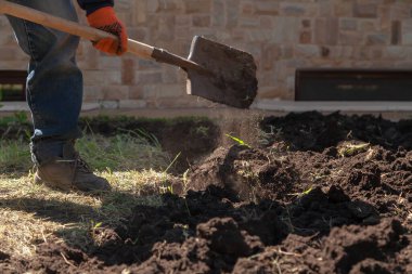 Kot pantolonlu bir adam kürekle toprağı kazıyor. Kuru otlar homurdanıyor