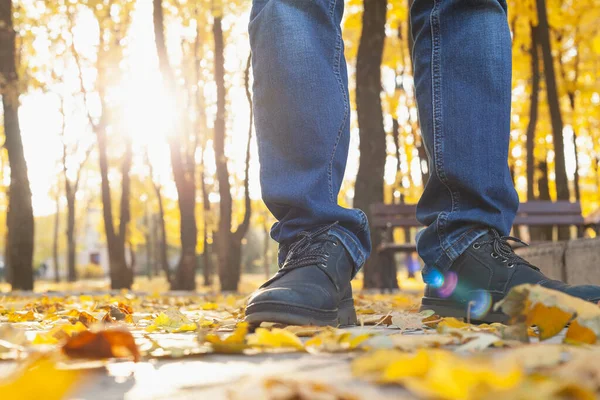 秋日漫步一个穿着蓝色牛仔裤和靴子的男人的腿站在秋天街上的铺板上 阳光正透过树干从后面灿烂地照耀着 — 图库照片