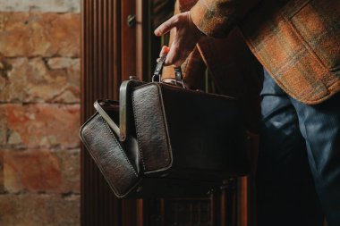 Gösterişli ekose ceketli bir beyefendi, evdeki eski moda bir çantayı açıyor.