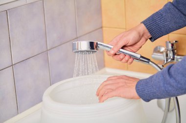 hand holds a shiny shower head and pours water into a round plastic container. Close-u