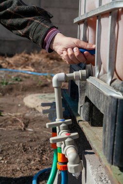 Sulama sistemi yönetimi. Bir el bahçe sulama sisteminin plastik borularından musluk açar. Su dolu bir konteynır borunun üstüne yerleştirildi.
