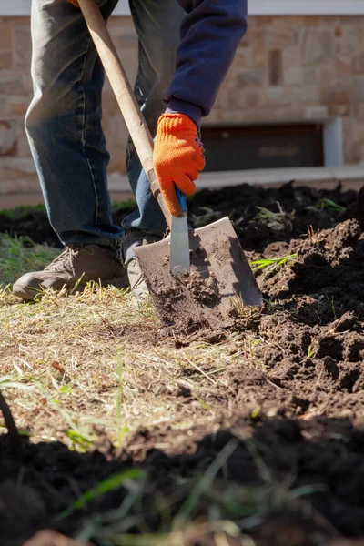 Hands in orange gloves cleaning a shovel from the ground using a narrow tool close-u