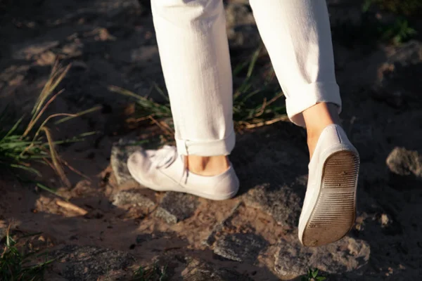 沿着海滩散步 在靠近你的沙滩上 穿着白色长裤和鞋子的女人的腿在石头上穿行 — 图库照片
