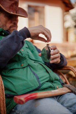 Oturan ve içinde alkol olan metal bir matarayı açan adamın silueti.