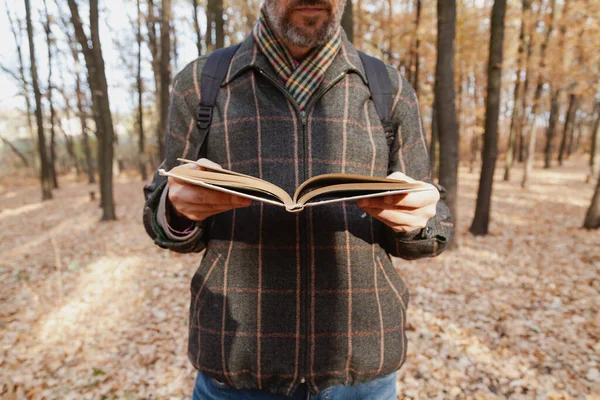 Man in a plaid jacket reading a book in the autumn fores