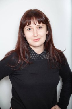 Pretty young woman in a black sweater and striped shirt posing and looking into the frame on a light backgroun