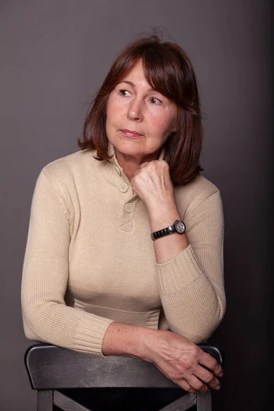 Portrait of a woman without retouching on a dark plain background. Elderly beautiful woman in a beige sweate