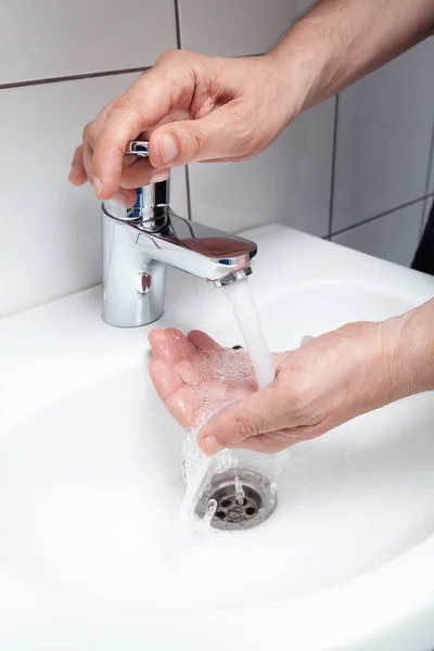 Sağ el, beyaz fayanslı lavabonun üstündeki musluğu açar. Sol eline bir su püskürtüsü dökülüyor. Beyaz fayanslar geliyor.