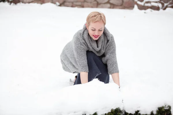穿着暖和毛衣的金发美女坐在院子里 手里拿着雪 — 图库照片