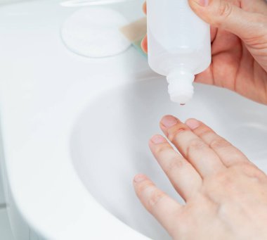 The right hand pours antiseptic on the injury on the middle finger of the left hand. The procedure is carried out under sterile conditions over a white tiled sin