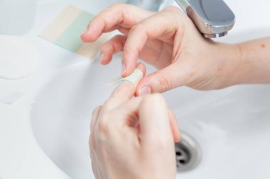 Prevention of small cuts of the hand. The right hand sticks a narrow strip of a bactericidal patch on the middle finger of the left hand. Close-u