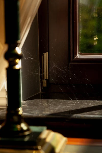 silvery spider web glows in the sun in the corner of a modern window and sill. In the foreground is a table lam