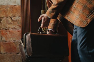 Gösterişli ekose ceketli bir beyefendi, evdeki eski moda bir çantayı açıyor.