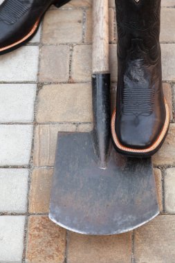 Black men cowboy-style leather boots stand on a shovel on paving slab