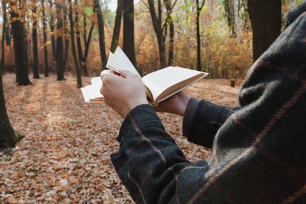 Hands turn over the pages of an open book in the autumn forest close-u