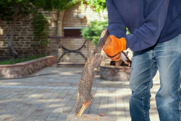 We prepare firewood for the barbecue. Hands in orange gloves chop a log on a stump with an ax on a sunny da