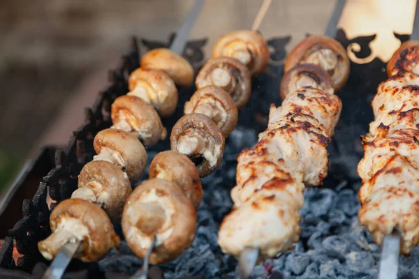 Grilling a barbecue. On a metal grill lies a row of skewers with mushrooms and pieces of mea