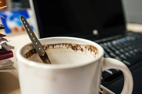 Tazza di caffè con cucchiaino all'interno con coperchio del computer portatile aperto in background — Foto Stock
