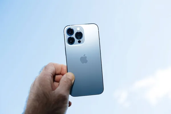 Ruční držení nejnovější Apple Computers iPhone 13 pro se všemi třemi zadními kamerami a lidar senzor proti modré obloze — Stock fotografie