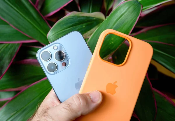 男子手持绿色植物背景新苹果电脑iPhone 13亲塞拉蓝色和橙色硅胶外壳 — 图库照片