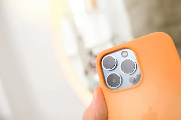 नारिंगी सिलिकॉन संरक्षण प्रकरण आणि तिन्ही मागील कॅमेरासह नवीनतम ऍपल संगणक आयफोन 13 प्रो धारण पीओव्ही नर हात बंद-अप — स्टॉक फोटो, इमेज