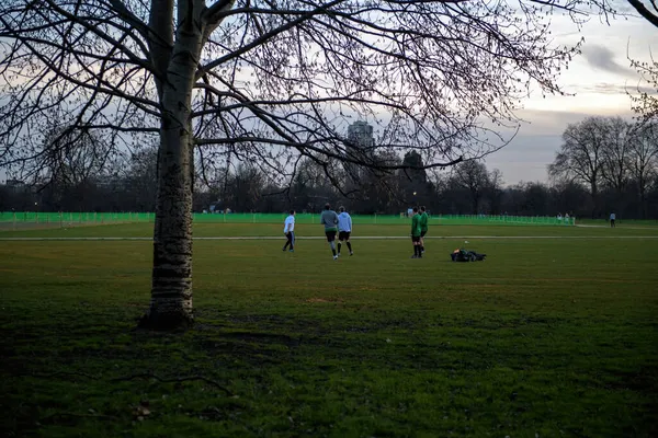 People playing football soccer at dusk in green British park — Stock Photo, Image