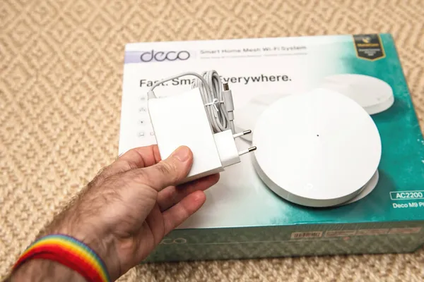 POV männliche Hand hält neuen Netzadapter für das Deco AC220 M9 Plus Tp-Link Internet Smart Home Wifi System nach dem Auspacken — Stockfoto