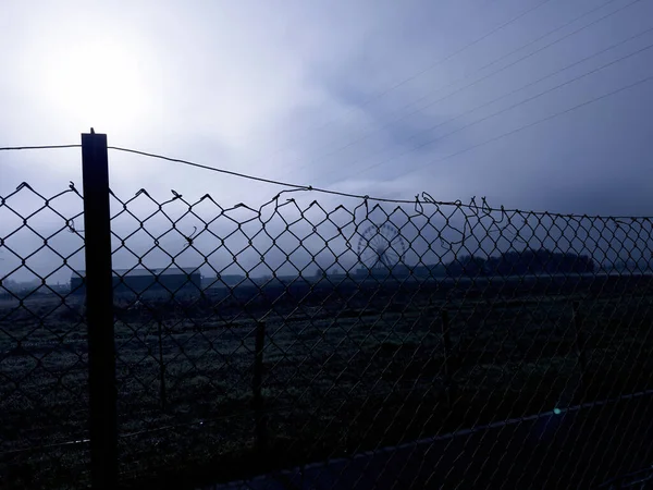 安全栅栏带刺铁丝网，有大片田野和旋转木马，在雾气中看到的背景下旋转 — 图库照片