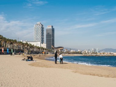 Barceloneta Plajı manzarası. İnsanlar Kasım ayında gökdelen ofis kulesiyle güneşleniyor.