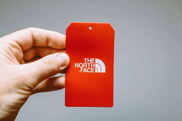 POV male hand holding etiquette sticker of The North Face paper documents backpack — 图库照片