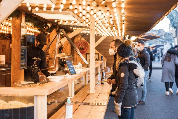 Pareja joven comprando deliciosos CHristmas Market comida alsaciana en el mercado chalet puesto — Foto de Stock