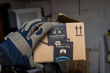 Male hand in protection glove holding in warehouse Amazon Cardboard box with Christmas Logotype