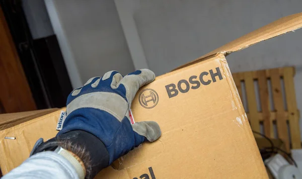 Male hand in protection glove holding in warehouse cardboard package box with Bosch Industrial insignia — ストック写真