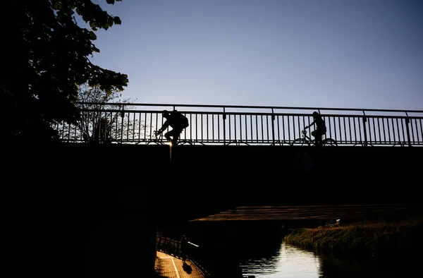 Low angle view of cyclists silhouettes on the bridge with clear blue sky behind them — Stock Photo, Image
