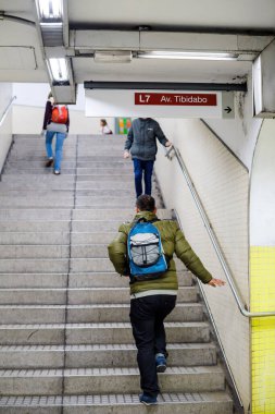Arkadaki görüntüde mavi sırt çantalı bir erkek metro metro istasyonunda talimatlarla yürüyor.