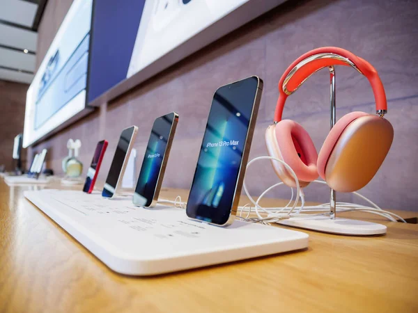 Fila de toda la línea actual de teléfonos inteligentes Apple Computers iPhone con auriculares AirPods Max de color rosa rojo —  Fotos de Stock