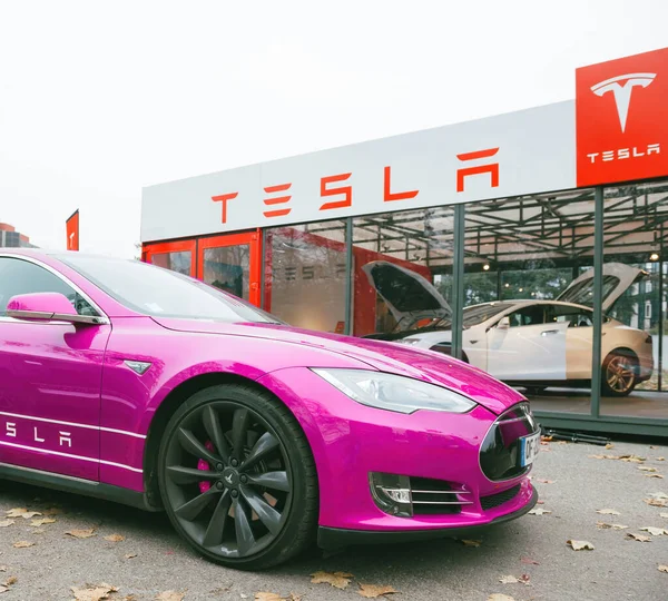 Nova fúcsia colorido Tesla Motors Modelo S carro estacionado perto de uma concessionária moderna de vidro — Fotografia de Stock