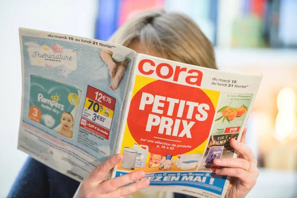 Vrouw die Cora hypermarket speciale aanbieding flyer leest door de beste prijzen te kiezen — Stockfoto