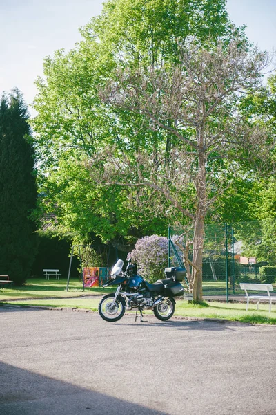 Pojedynczy motocykl BMW zaparkowany przed zielonym parkiem z kwitnącymi drzewami w tle — Zdjęcie stockowe