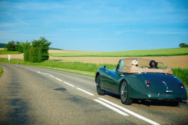 Defocused view of rear view couple inside vintage green unrecognizable car drigin on the rural road — Stock Photo, Image